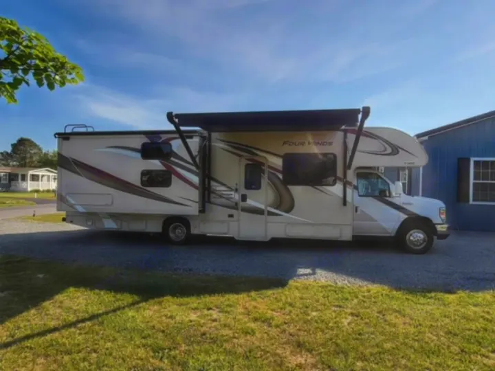 Beige and white Four Winds motorhome RV rental parked on gravel with awning extended.. Thor Four Winds 2020