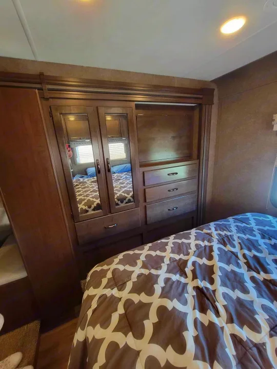 This RV rental bedroom features a comfy bed, mirrored wardrobe, and dresser, offering comfort and storage for your travels.. Thor Four Winds 2020