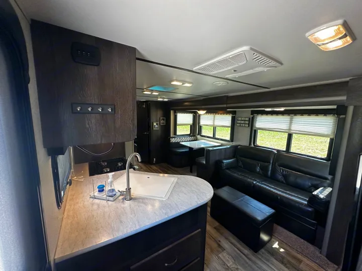 Spacious RV rental interior featuring a full kitchen, dinette, and comfortable living area with a black leather sofa.. Keystone RV Outback Ultra-Lite 2018