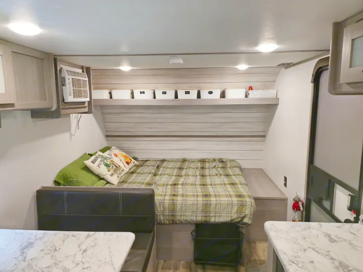 Inside this RV rental: a cozy space with a plaid bed, dinette, AC, and clever labeled storage bins overhead.. Dutchmen Coleman Lantern LT 17B 2024