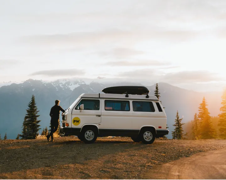 RV rental adventure: White camper van and person by snow-capped mountains at sunset, bathed in golden light.. Volkswagen Westfalia 1990