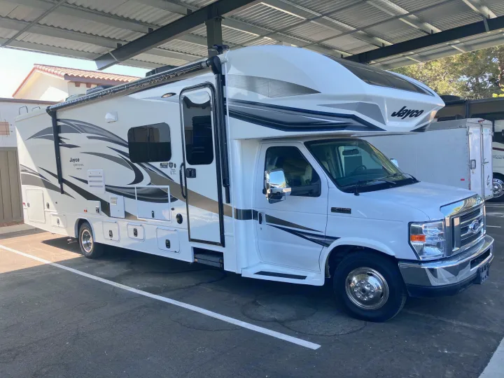 Bright white Jayco Class C motorhome, available for rv rental, parked in a covered outdoor lot.. Jayco Insignia 2018