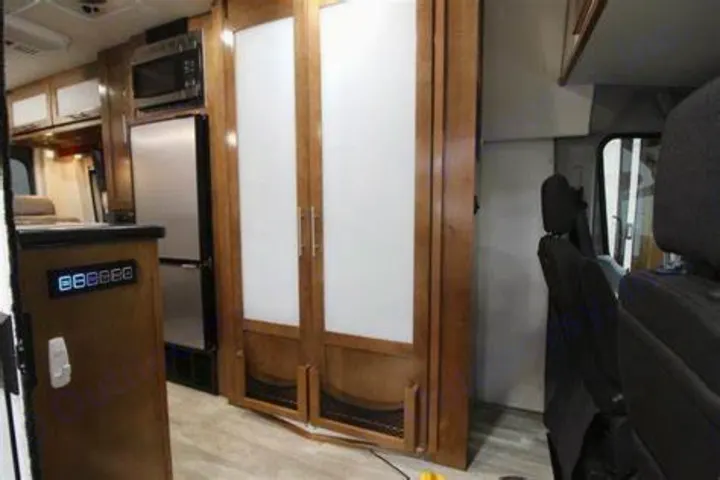 Inside this RV rental, see the kitchen area with microwave/fridge, wooden cabinets, and front vehicle seating.. Forest River Coachmen Crossfit 2018