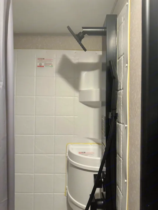 An RV rental bathroom interior featuring a black multi-function shower panel with a fixed head and handheld sprayer.. Forest River Cherokee Wolf Pup Black Label 2022