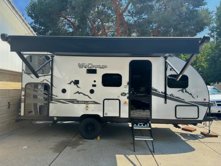 White Black Label Wolf Pup travel trailer RV rental, with awning extended and steps down, perfect for camping.. Forest River Cherokee Wolf Pup Black Label 2022