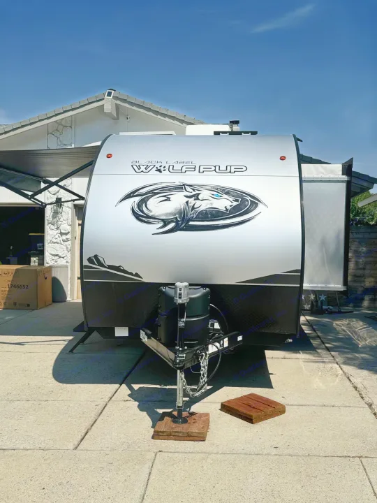 Black Label Wolf Pup travel trailer, potentially an RV rental, parked on a sunny driveway at a house.. Forest River Cherokee Wolf Pup Black Label 2022