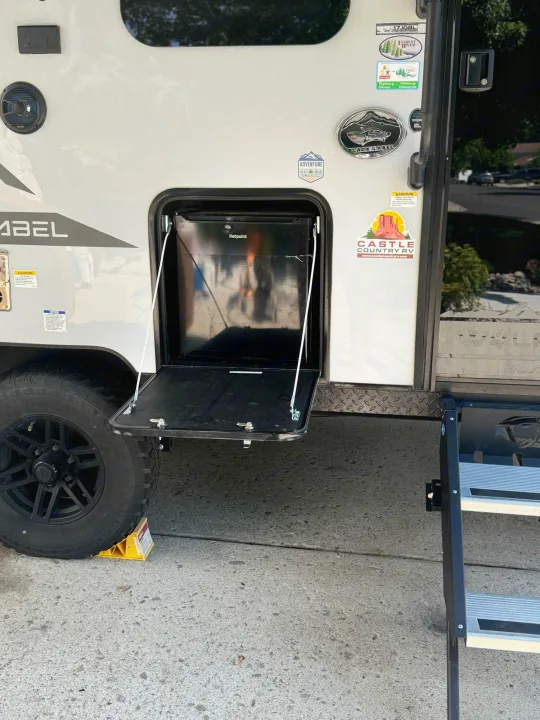 RV rental travel trailer side with open compartment, Hotpoint fridge, wheel chock, and steps.. Forest River Cherokee Wolf Pup Black Label 2022
