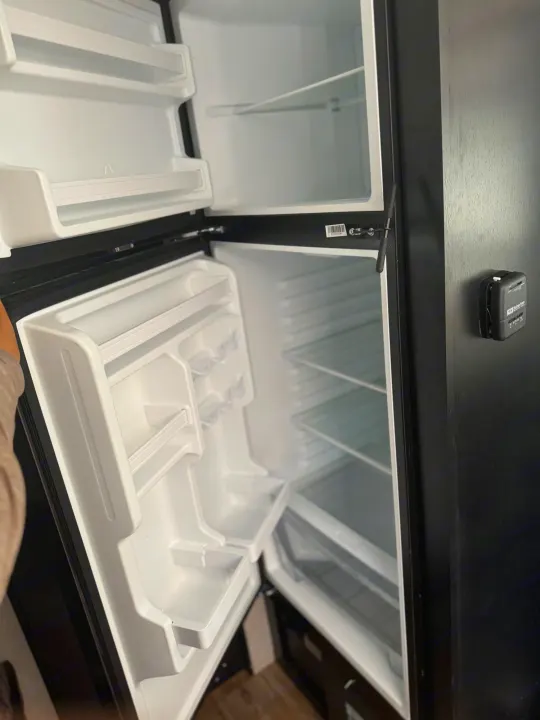 Clean, empty refrigerator and freezer in an RV rental, showcasing shelves, door bins, and a Suburban thermostat. Ready for your adventure!. Forest River Cherokee Wolf Pup Black Label 2022