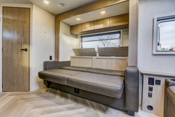 Modern rv rental interior: sofa bed, herringbone floor, wooden door, window with storage, and convenient outlets.. Ember Overland 2023