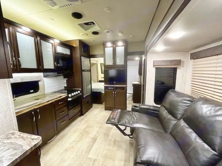 Inside a modern RV rental: a bright, spacious interior showing kitchen, living area with recliners, and a bedroom.. Grand Design Momentum 2020