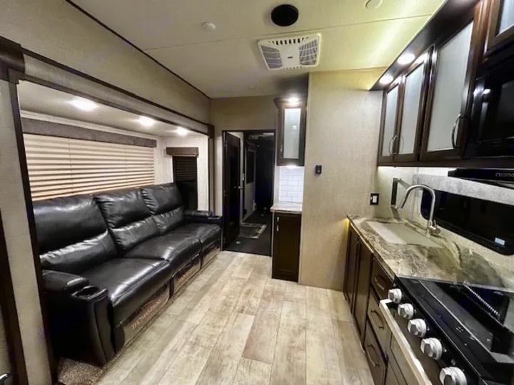 This spacious RV rental interior features a comfy black leather sofa, full kitchen with modern appliances, and wood-look flooring.. Grand Design Momentum 2020