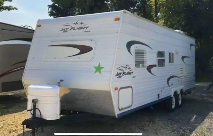 White Jayco Jay Flight RV rental, a travel trailer with green star decal, parked on gravel.. Jayco Jay Flight 2005