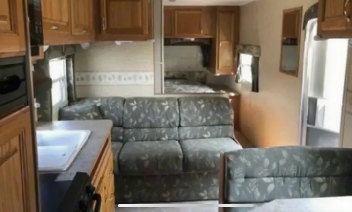 Compact RV rental interior featuring a kitchen with sink, L-shaped sofa, dining area, and raised bed.. Jayco Jay Flight 2005