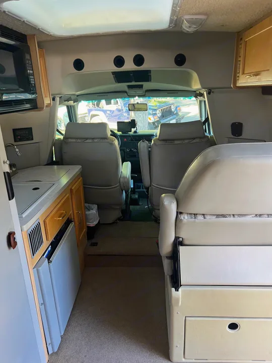 RV rental interior shows a kitchenette, microwave, front cockpit, and rear seating areas.. Winnebago Rialta 2003