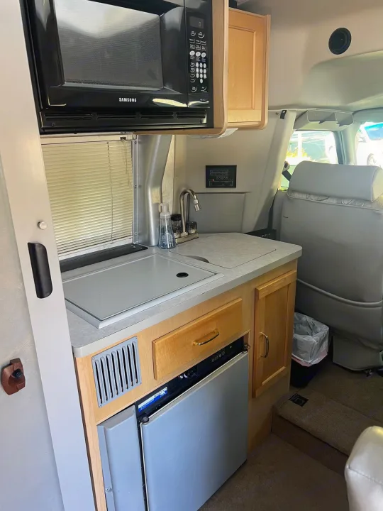 Inside an RV rental: a compact kitchen with microwave, sink, refrigerator, and ample storage for trips.. Winnebago Rialta 2003