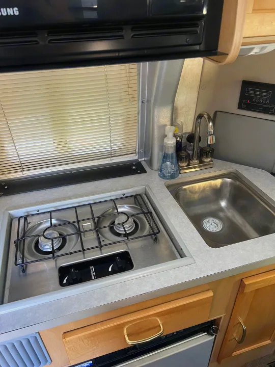 This RV rental offers a well-equipped compact kitchen, complete with a gas stove, sink, and refrigerator.. Winnebago Rialta 2003
