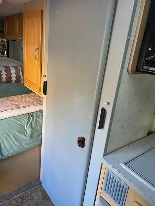Inside an RV rental, showing the compact living space with a bed, kitchen counter, and refrigerator.. Winnebago Rialta 2003