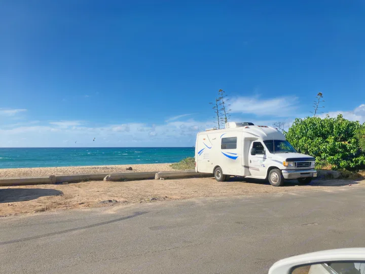 Enjoy this RV rental adventure! White Class C RV parked beachfront, with blue ocean & sky, and kitesurfers.. Ford Econoline 2004