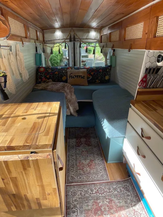 This cozy RV rental's custom van interior features a U-shaped lounge, wooden accents, and a compact kitchen.. Ford Transit 2019