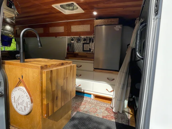 Inside an RV rental: a well-equipped mobile kitchen with wood details, fridge, and ample storage for adventures.. Ford Transit 2019
