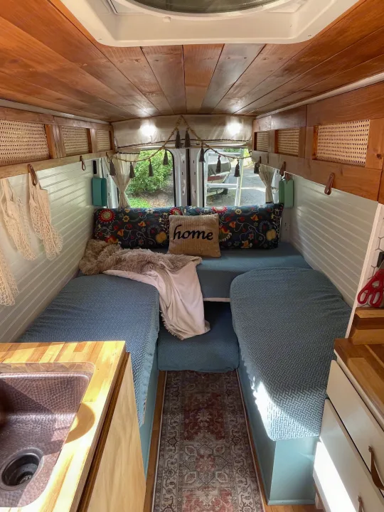 Cozy RV rental interior with wooden ceiling, comfortable seating, and a compact kitchen sink. Perfect for van life adventures.. Ford Transit 2019