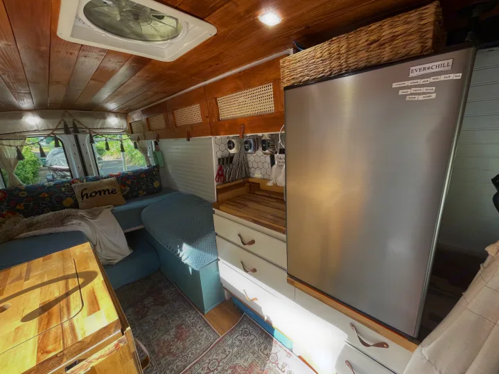 Explore this stylish RV rental! Cozy camper van interior with wood ceiling, kitchen, fridge, storage, and comfy seating area.. Ford Transit 2019