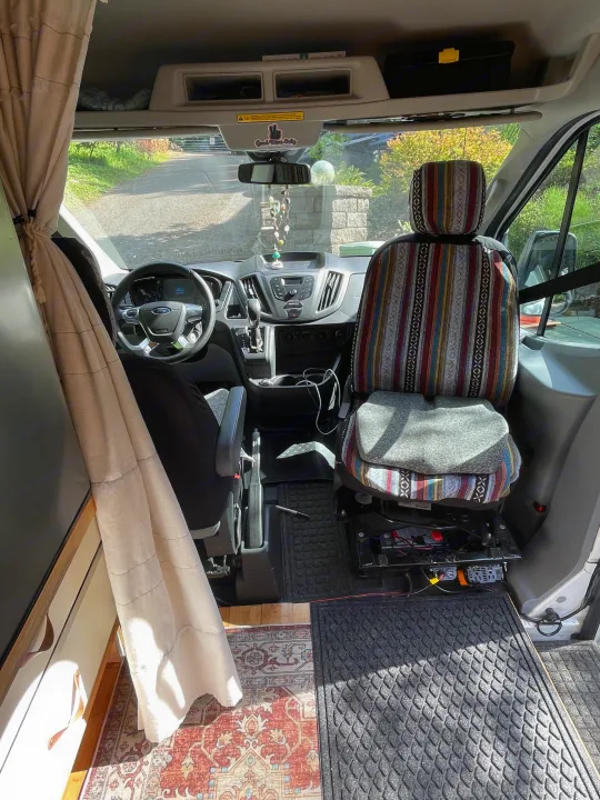 View inside a Ford camper van RV rental, showing the front cabin with two seats, dashboard, and custom interior.. Ford Transit 2019
