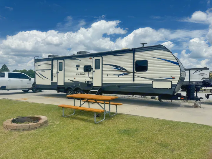 This travel trailer RV rental is set up at a campsite with a picnic table & fire pit under a blue sky with clouds.. Forest River Palomino Puma 2018