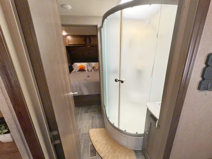 This RV rental offers a cozy bedroom seen through an open door, and a modern bathroom with a curved shower and sink.. Forest River Palomino Puma 2018