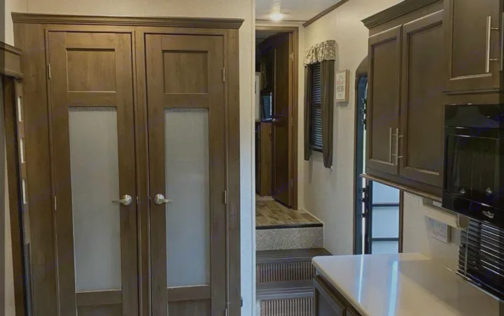 Explore this RV rental: modern interior with dark wood cabinets, frosted doors, and split-level living space.. Keystone Cougar 2020