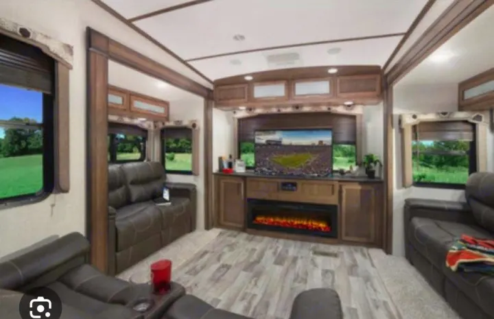 RV rental interior: A spacious living area with brown recliners, large TV, and electric fireplace. Scenic windows.. Keystone Cougar 2020