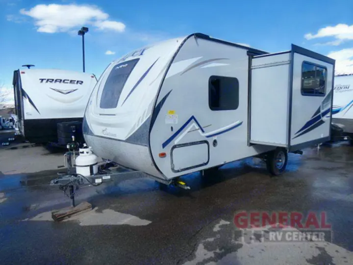 A light-colored travel trailer with its slide-out extended is parked at a dealership, ready for RV rental. Another RV is behind it.. Coachmen Apex Nano 2018