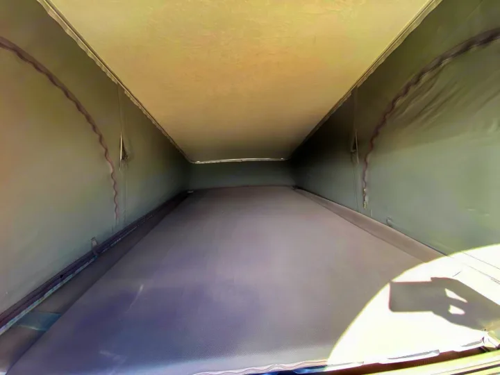 Inside an RV rental pop-top, a spacious sleeping area features a mattress and light-colored fabric walls and ceiling.. Adria Mode 2024