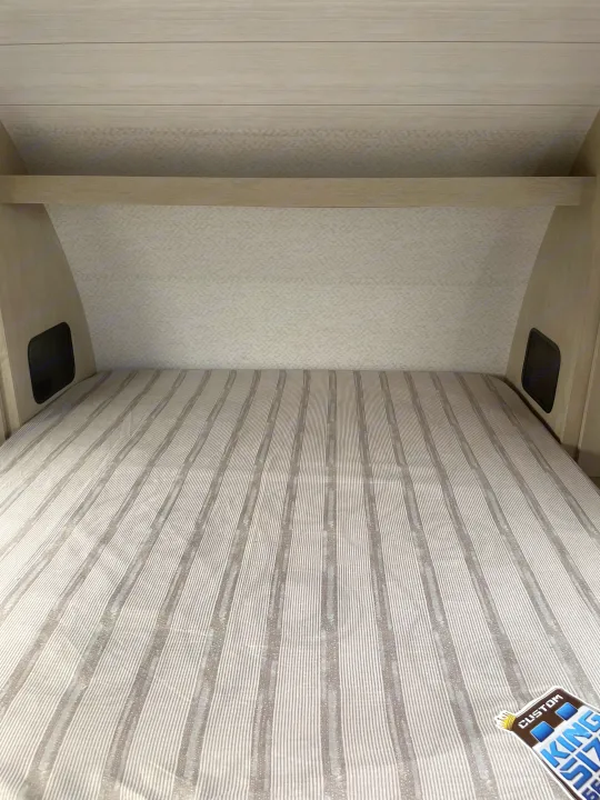 RV rental sleeping area featuring a striped bed, light wood paneling, and practical built-in side storage.. Forest River Wildwood X-Lite 2023