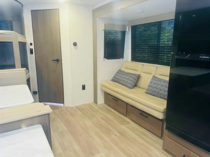 Explore this clean RV rental interior! Features include bunk beds, a cozy sofa with storage, and an entertainment unit.. Grand Design Transcend Xplor 2024