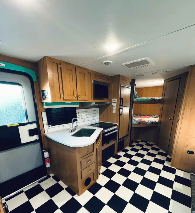 Inside this rv rental: compact kitchen, bunk beds, and black & white floor. Perfect for family adventures.. Riverside RV Retro 2023