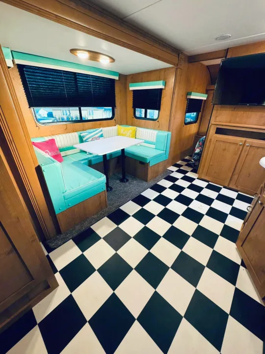 Explore this vibrant rv rental interior! A retro teal dinette, wood paneling, and checkered floor define this cozy camper.. Riverside RV Retro 2023