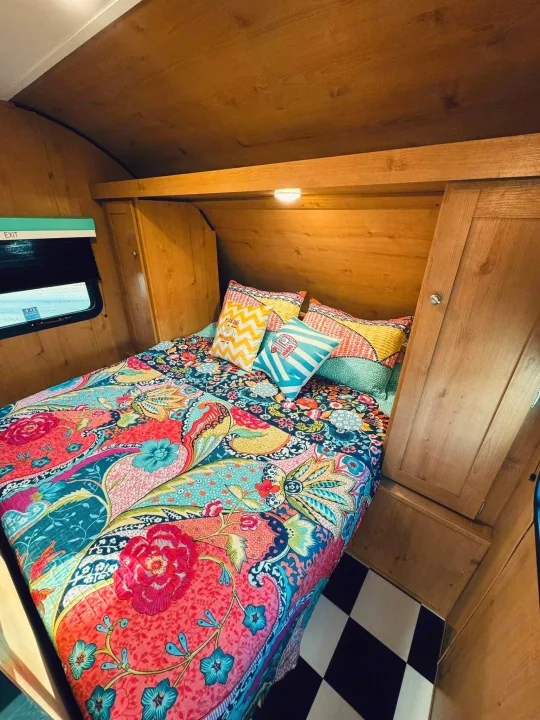 Vibrant, colorful bed inside a cozy RV rental bedroom with wood paneling and a checkered floor.. Riverside RV Retro 2023