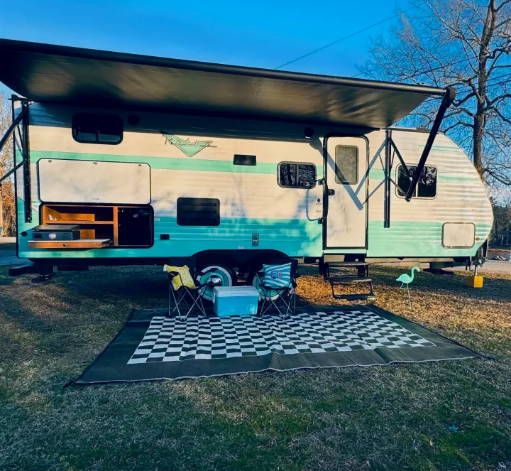 Cozy retro RV rental set up for outdoor living with an awning, kitchen, chairs, and rug. Perfect for camping!. Riverside RV Retro 2023