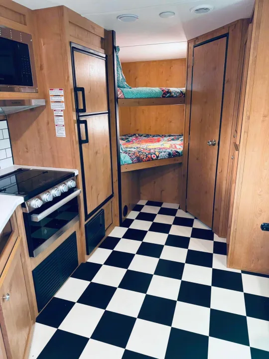 An RV rental interior showing a kitchen, refrigerator, bunk beds, and black & white checkered floor.. Riverside RV Retro 2023