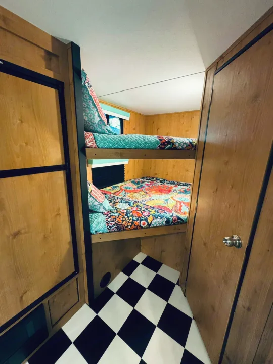 Cozy RV rental interior with colorful stacked bunk beds & checkered floor, ideal for family travel.. Riverside RV Retro 2023