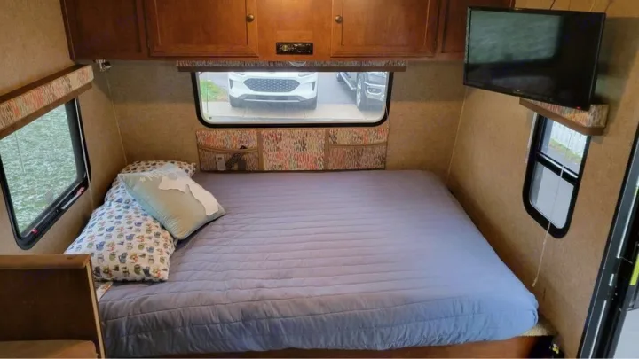 Cozy RV rental bedroom with a comfy bed, overhead cabinets, windows, and TV, ready for your next adventure.. Spree Escape 2016