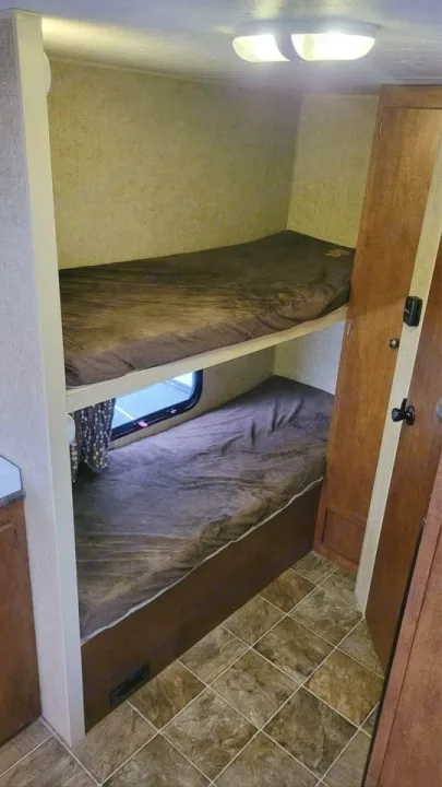 Cozy RV rental bunk beds, two dark brown sleeping areas one above the other, with a window in a compact RV interior.. Spree Escape 2016