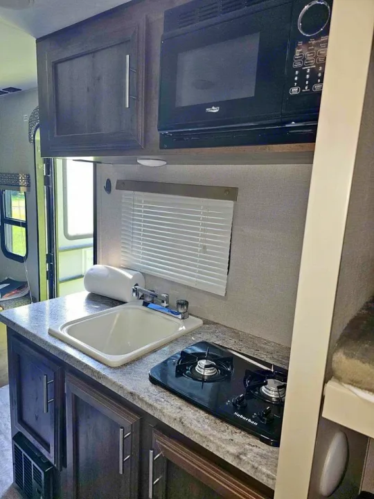 This RV rental kitchen features a sink, 2-burner stovetop, microwave, and dark wood-look cabinet storage.. Spree Escape 2016