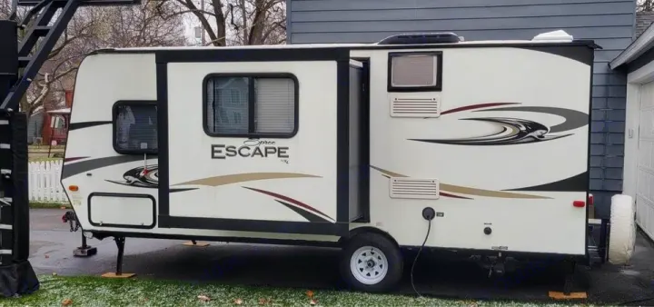 White "Spree Escape" travel trailer (RV rental) set up with stabilizers, showing windows, door, and exterior graphics.. Spree Escape 2016