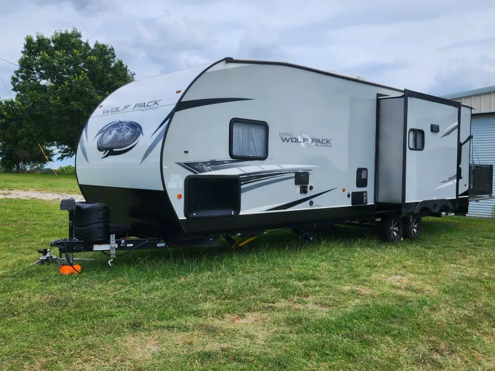 Modern gray Cherokee Wolf Pack Platinum toy hauler RV rental on green grass, ready for outdoor adventures.. Forest River Wolf Pack 2023