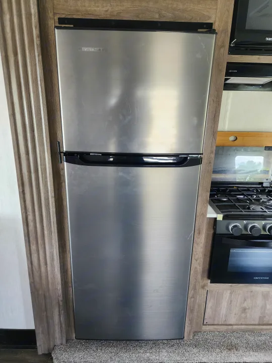 Stainless steel refrigerator and gas oven in an RV rental kitchen, offering essential amenities for travel.. Forest River Wolf Pack 2023