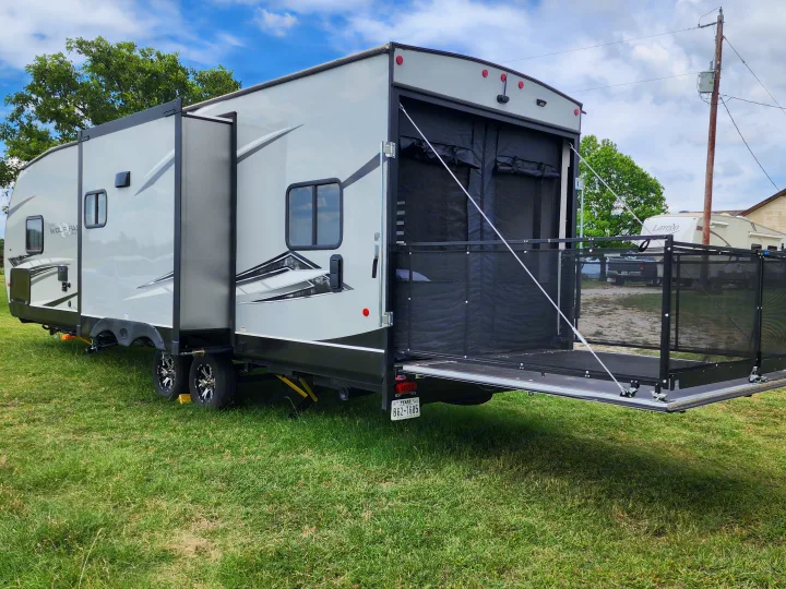 Spacious gray toy hauler RV rental with slide-out and rear patio deck on grass. Perfect for camping and outdoor adventures.. Forest River Wolf Pack 2023