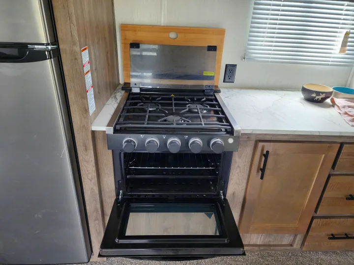 Inside an RV rental: a neat kitchen featuring a gas stove, open oven, fridge, and ample counter space for travelers.. Forest River Wolf Pack 2023