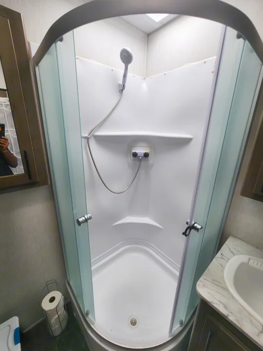 Step inside this RV rental's corner shower, featuring a handheld shower head, control knobs, and glass enclosure.. Forest River Wolf Pack 2023